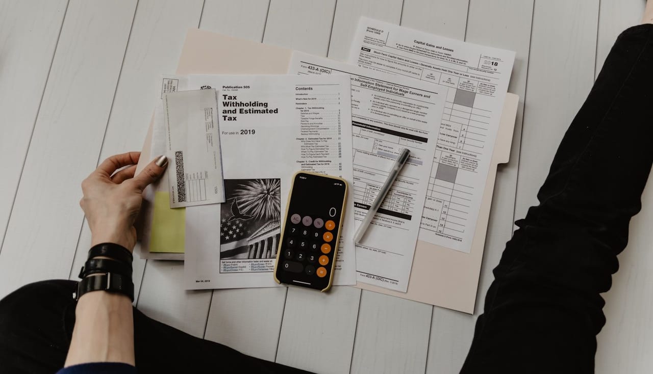 A person compares figures across printed forms with a calculator and pen.